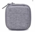 Grey portable cable organizer bag open on a white surface next to a laptop showing stored charger and cables.