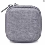 Grey portable cable organizer bag open on a white surface next to a laptop showing stored charger and cables.